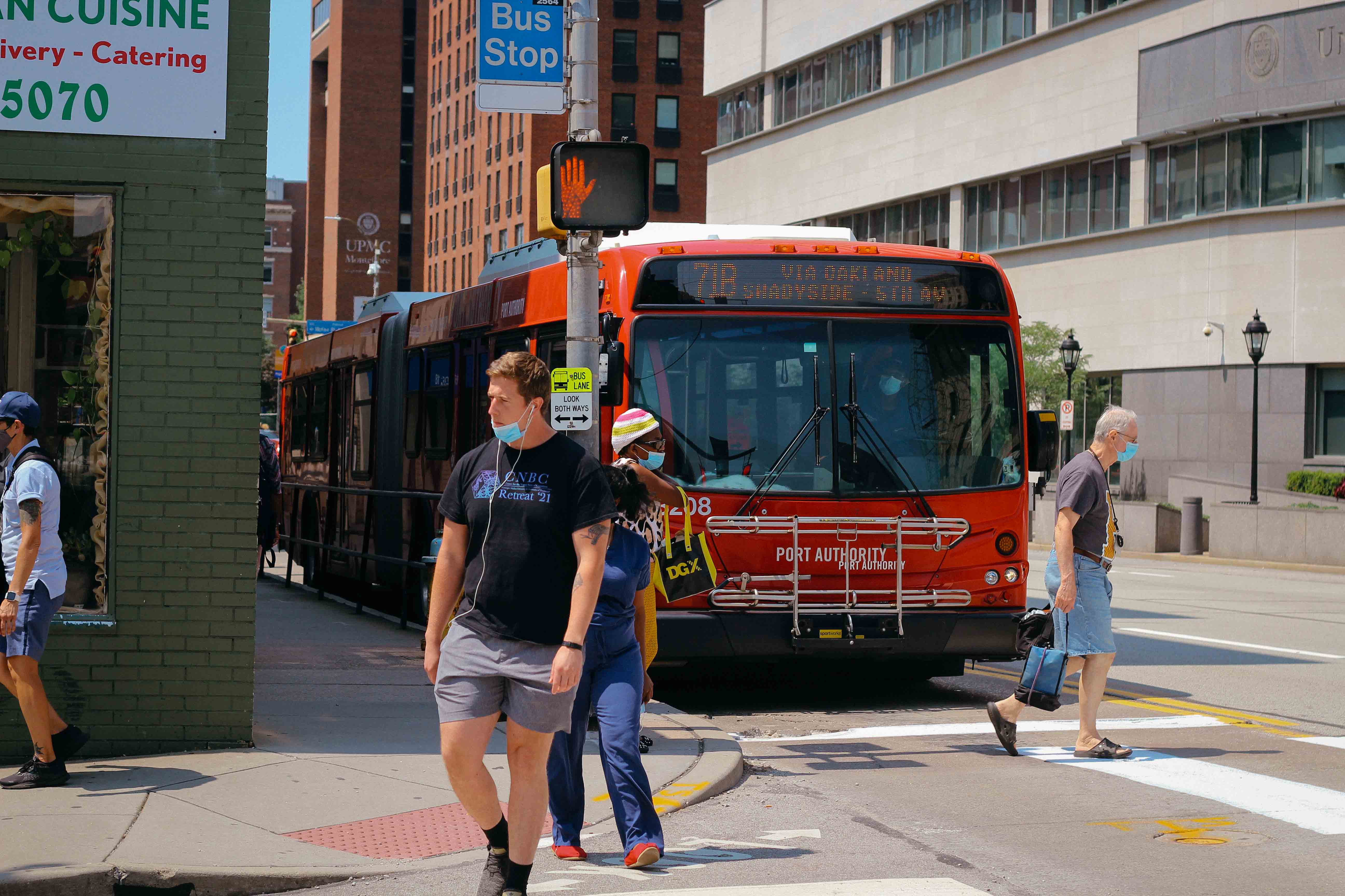 Variety of people walking in OBID on sunny day with bus in background