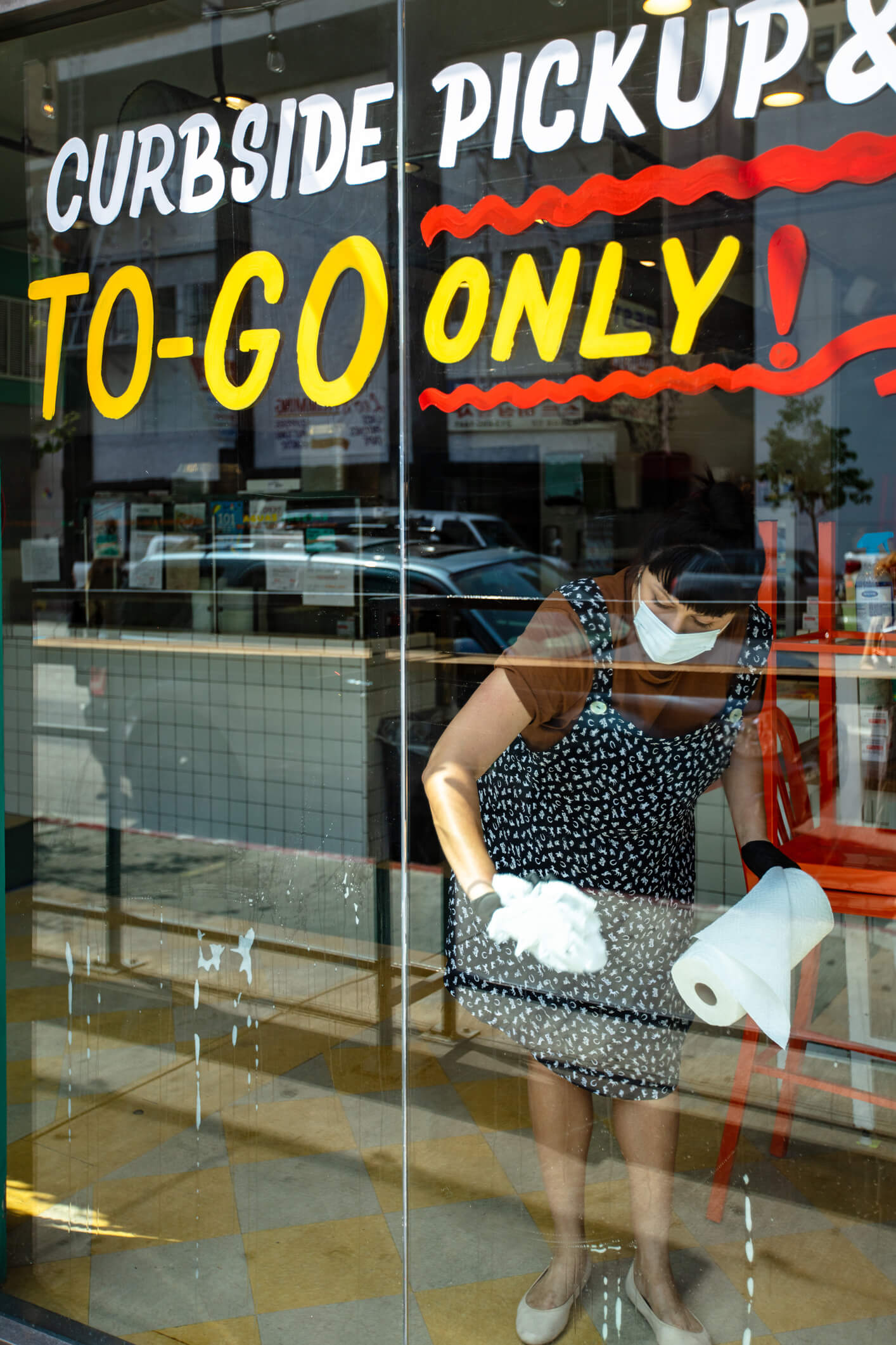 Woman with mask at restaurant cleaning storefront glass